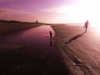 Man walking on beach against sky during sunset