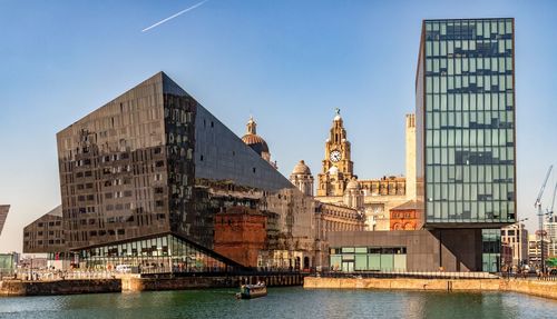 View of buildings by river against sky in city