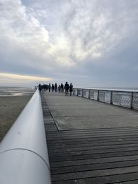 People on railing by sea against sky