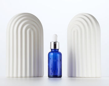 Blue glass bottle with a pipette and white decorative arches on a white background. template for 