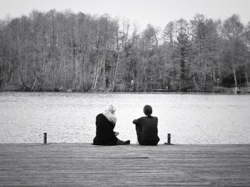 Rear view of man sitting on bench by lake