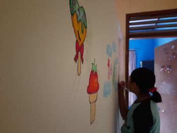 Rear view of boy standing against wall at home