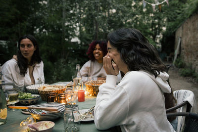 Side view of woman laughing while sitting at dining table during dinner party