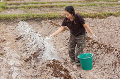 Woman putting fertilizer while standing on agricultural field