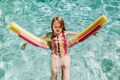 Young girl floating on her back in pool with pool noodles