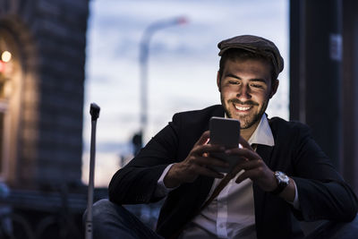 Smiling young man in the city checking cell phone in the evening