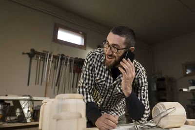 Happy craftsperson talking on smart phone at workbench