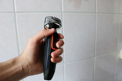 Close-up of man holding electric razor against white tile wall in bathroom