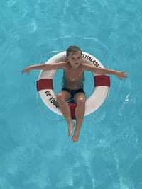 High angle portrait of smiling boy swimming in pool with lifebuoy