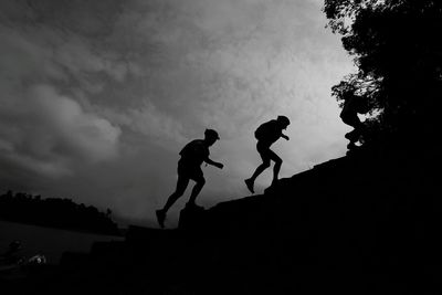 Low angle view of silhouette people walking on mountain against cloudy sky at dusk