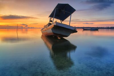 Boat moored in sea against sky during sunset