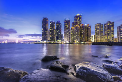 Sea by illuminated buildings against sky at night