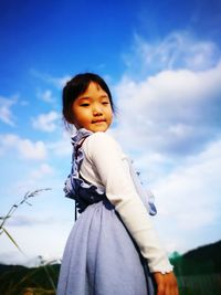 Low angle view of girl standing against blue sky