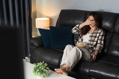 Low angle view of woman using phone while sitting on sofa at home
