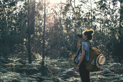 Side view of woman photographing in forest