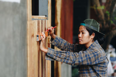 Side view of young female carpenter taking measurement of wood