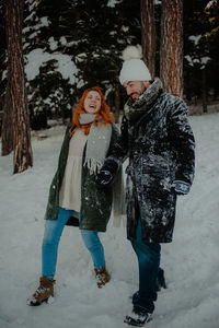 Smiling couple holding hands walking on snow covered land in forest