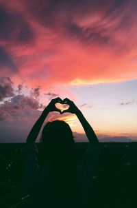 Rear view of silhouette woman with heart shape against sky during sunset