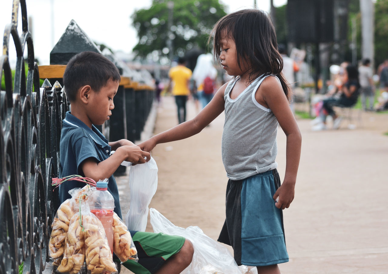 child, childhood, girls, innocence, real people, females, women, males, men, family, togetherness, two people, boys, focus on foreground, side view, incidental people, three quarter length, sibling, leisure activity, sister, outdoors