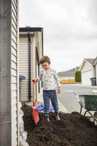 Young boy standing on pile of dirt, soil with shovel in back alley.