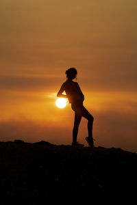 Silhouette woman standing on field against orange sky