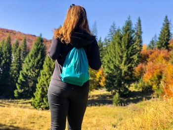 Rear view of woman with backpack standing on field against trees