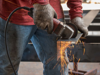 Midsection of man grinding metal at factory