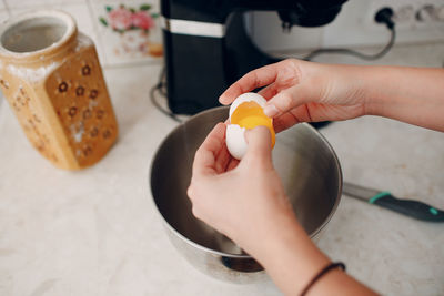 Cropped hands of woman breaking egg in kitchen