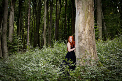 Woman standing by tree trunk in forest