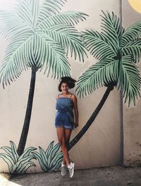 Portrait of young woman standing by palm tree
