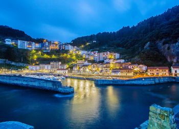 Illuminated buildings by river against sky in city