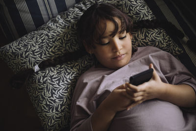 High angle view of girl using smart phone while lying down on bed at home