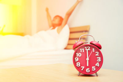 Close-up of alarm clock on table with woman relaxing on bed at home