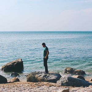 Man standing on rock by sea against clear sky