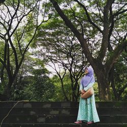 Woman in hijab standing against trees