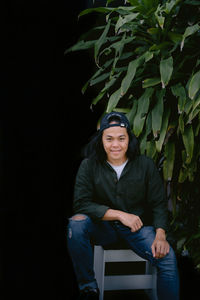 Portrait of young man sitting against black background