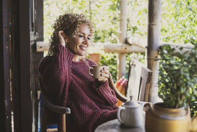 Smiling woman holding coffee cup sitting at balcony