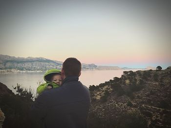 Rear view of father and son standing on beach against clear sky