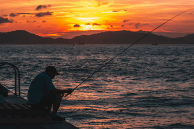 Man fishing in sea against orange sky