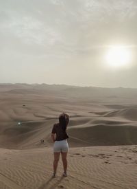 Rear view of woman standing on beach against sky