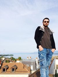 Portrait of young man standing on roof against sky