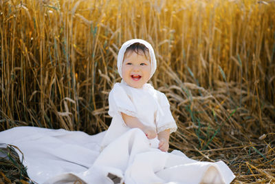 Sweet eight-month-old baby boy sitting on a blanket in a field and laughing