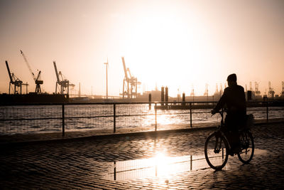 Silhouette man riding bicycle on city during sunset