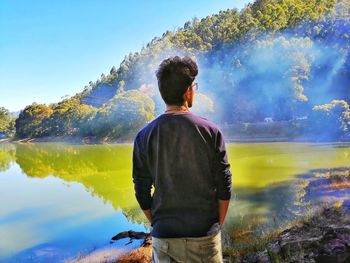 Rear view of man looking at lake against sky