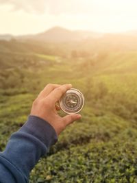 Cropped hand holding navigational compass against field