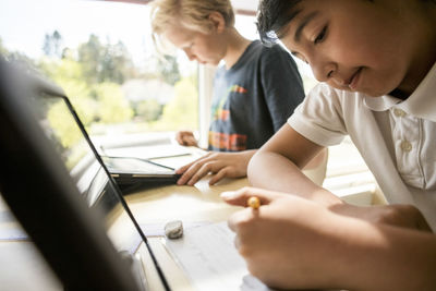 Boys e-learning from digital tablet against window in classroom