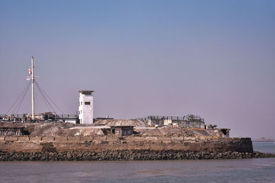 Lighthouse by sea against buildings against clear sky