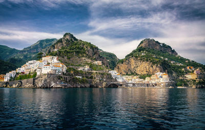 Houses on mountain by sea against cloudy sky