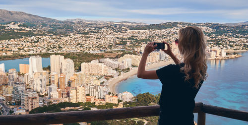 Rear view of woman photographing cityscape against sky