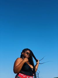 Low angle portrait of young woman standing against blue sky